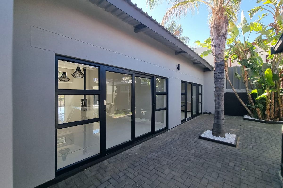 A modern rear exterior view featuring a paved patio area, black aluminium sliding doors, and well-maintained exterior finishes.