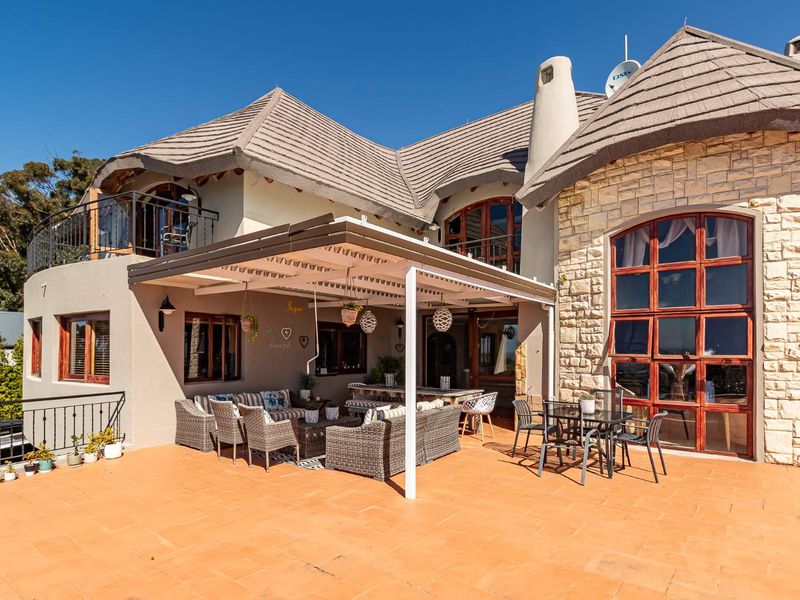 Spacious rear patio featuring a covered pergola, stone-clad exterior walls, and a distinctive thatched roof design with an upper-level balcony.