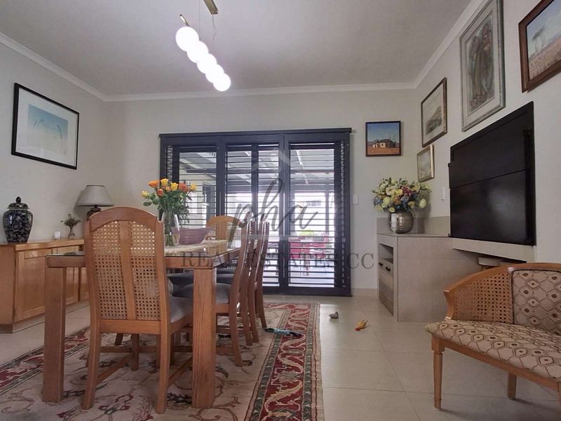 A well-maintained dining room featuring tiled flooring, cove cornicing, and secure sliding shutters leading to the outdoor area.
