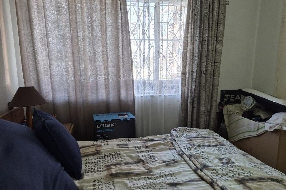 A bedroom featuring a window with security bars and curtains, providing natural light to the space.