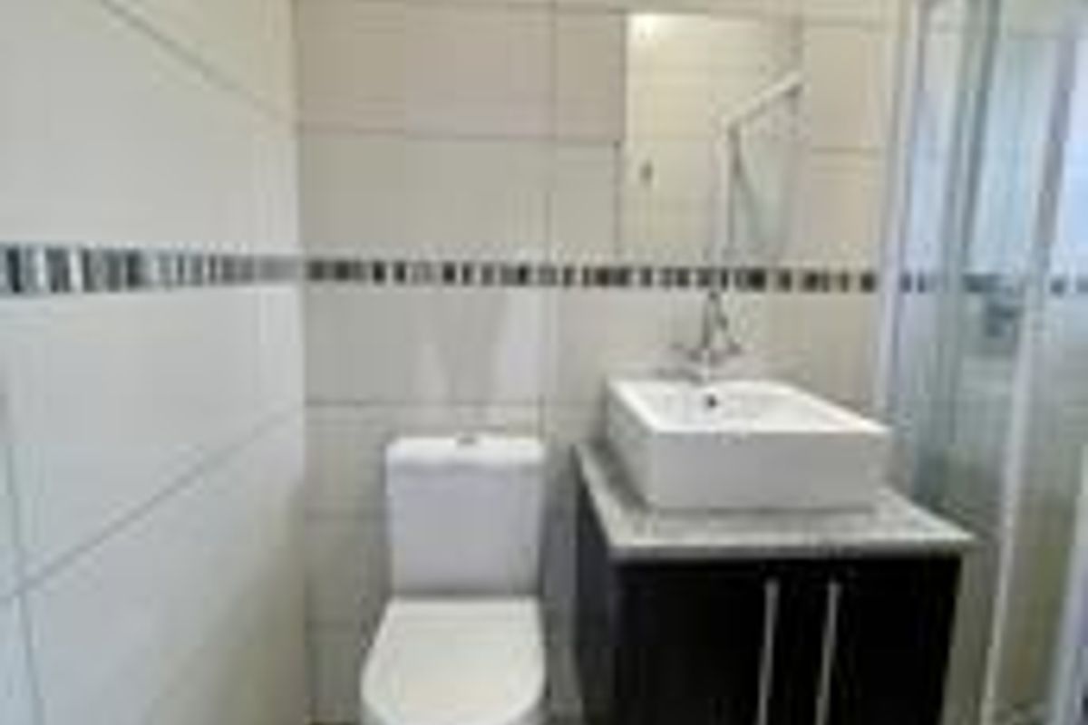 A clean, modern bathroom featuring a vessel sink on a dark vanity cabinet, a toilet, and a glass-enclosed shower with neutral wall tiling.