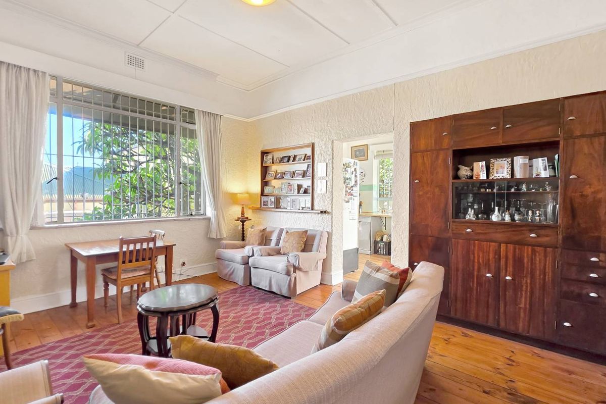 A living room featuring original timber flooring, built-in wooden cabinetry, and large windows with security bars, offering a classic and well-maintained aesthetic.