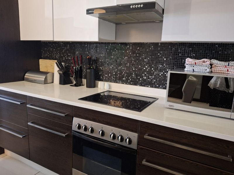 Modern kitchen featuring dark wood-grain cabinetry, white quartz countertops, a mosaic tile backsplash, and integrated stainless steel oven and extractor fan.