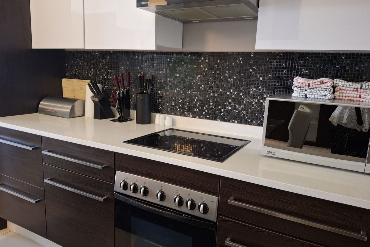 Modern kitchen featuring dark wood-grain cabinetry, white quartz countertops, a mosaic tile backsplash, and integrated stainless steel oven and extractor fan.