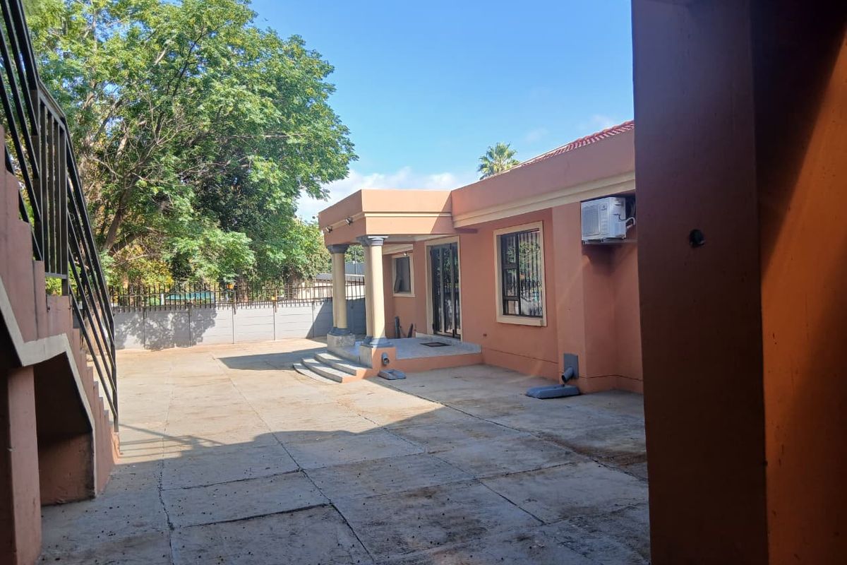 A view of the rear exterior area featuring a paved courtyard, covered patio entrance with columns, and external air conditioning unit.
