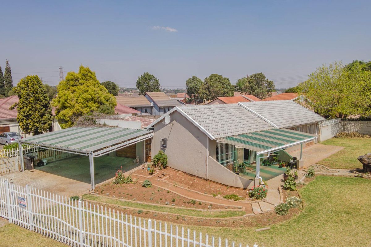 An elevated view of a residential property featuring a tiled roof, a double carport, a covered patio area, and a landscaped garden with perimeter fencing.