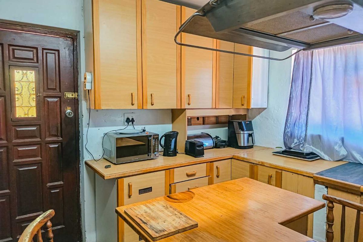 A functional kitchen featuring light wood-toned cabinetry, laminate countertops, and an integrated extractor fan, providing a practical workspace with direct access to an exterior door.