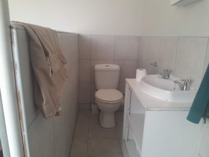 A functional bathroom featuring a standard toilet and vanity basin with tiled finishes, currently showing signs of wear and missing cabinetry components.