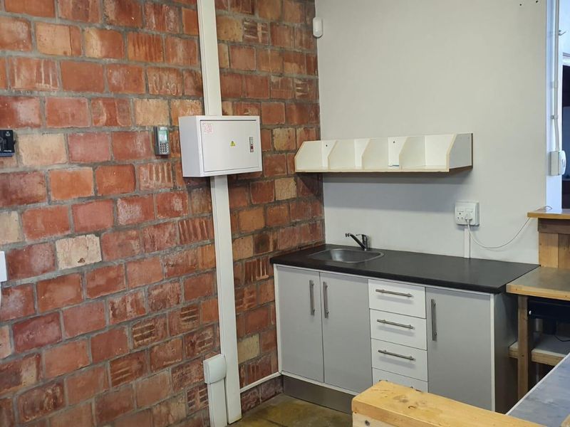 A functional utility space featuring exposed brickwork, built-in cabinetry with a sink, and wall-mounted storage shelving, suitable for a workshop or service area.
