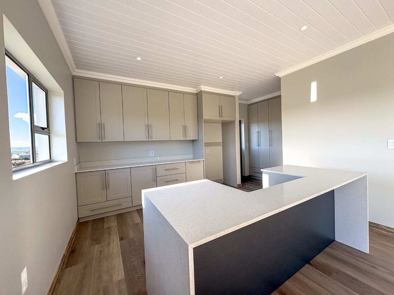 Modern kitchen featuring light grey cabinetry, stone countertops, a breakfast bar, and wood-look flooring under a white tongue-and-groove ceiling.