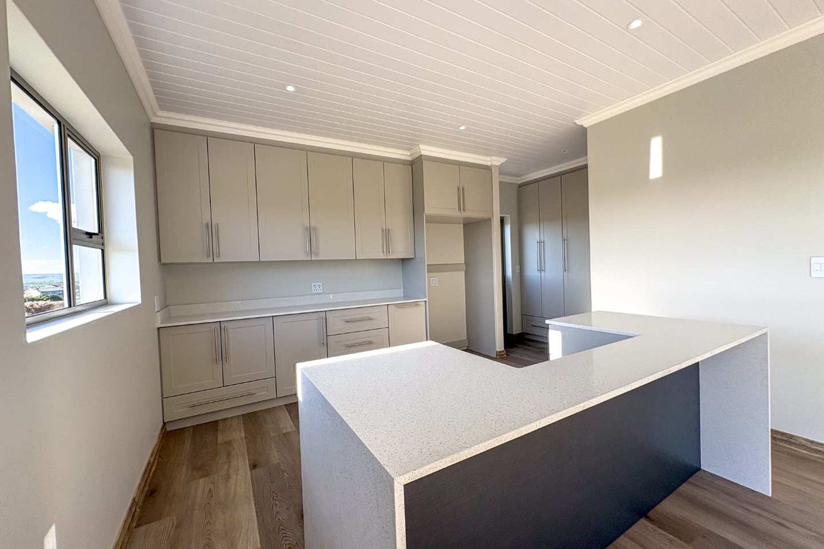 Modern kitchen featuring light grey cabinetry, stone countertops, a breakfast bar, and wood-look flooring under a white tongue-and-groove ceiling.