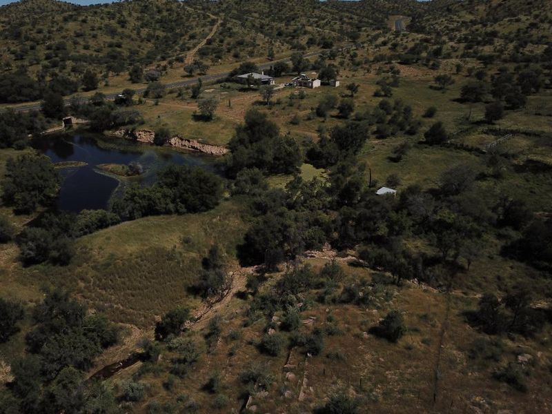 An aerial view of a large, undeveloped residential land parcel featuring natural vegetation, a water body, and proximity to a main road.