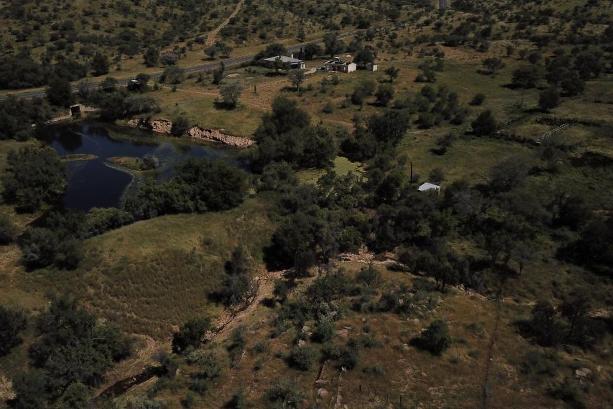An aerial view of a large, undeveloped residential land parcel featuring natural vegetation, a water body, and proximity to a main road.