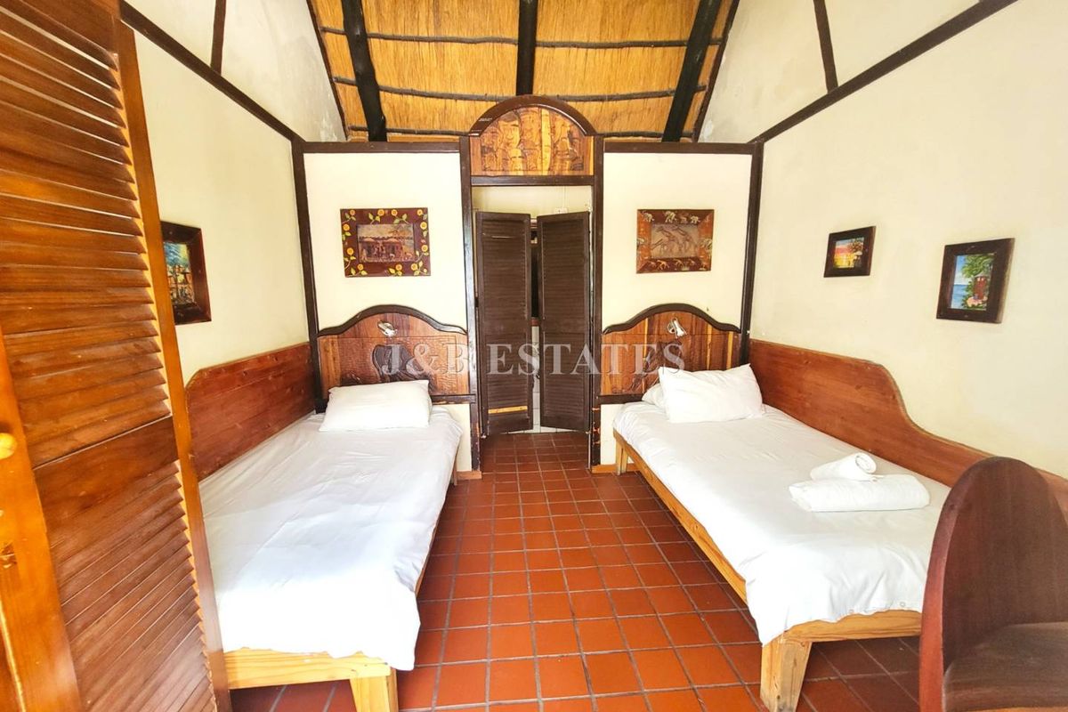 A rustic bedroom featuring a high thatched ceiling, terracotta tiled flooring, and built-in wooden headboards with integrated lighting.