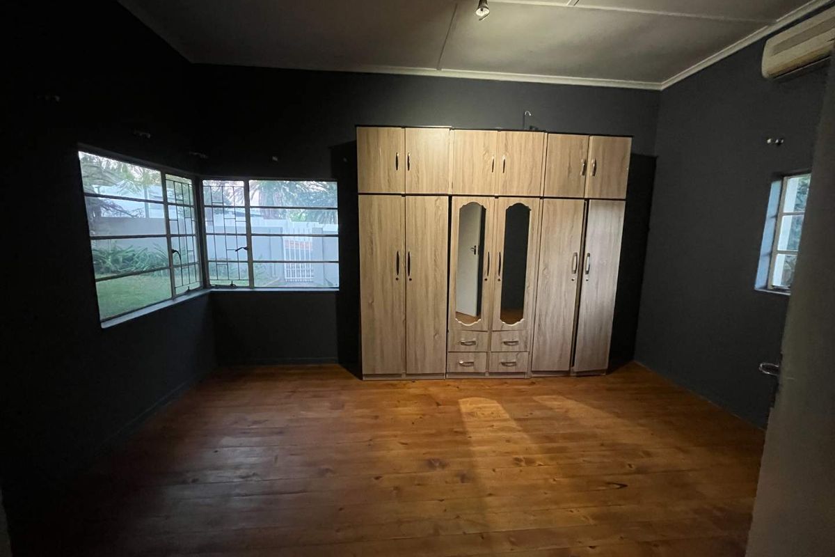 Spacious bedroom featuring dark painted walls, polished wooden flooring, and extensive built-in wooden cabinetry with integrated mirrors.
