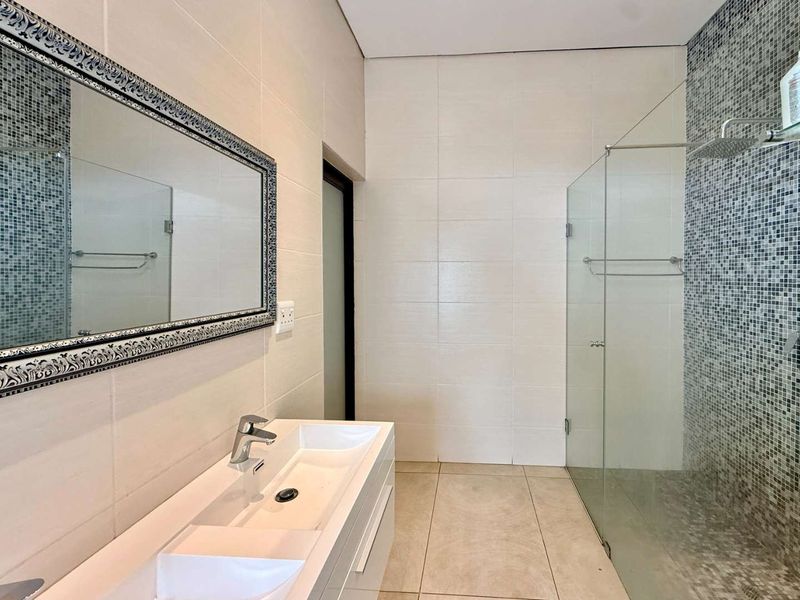 Modern bathroom featuring a double vanity, large framed mirror, and a spacious walk-in shower with a mosaic tile accent wall.