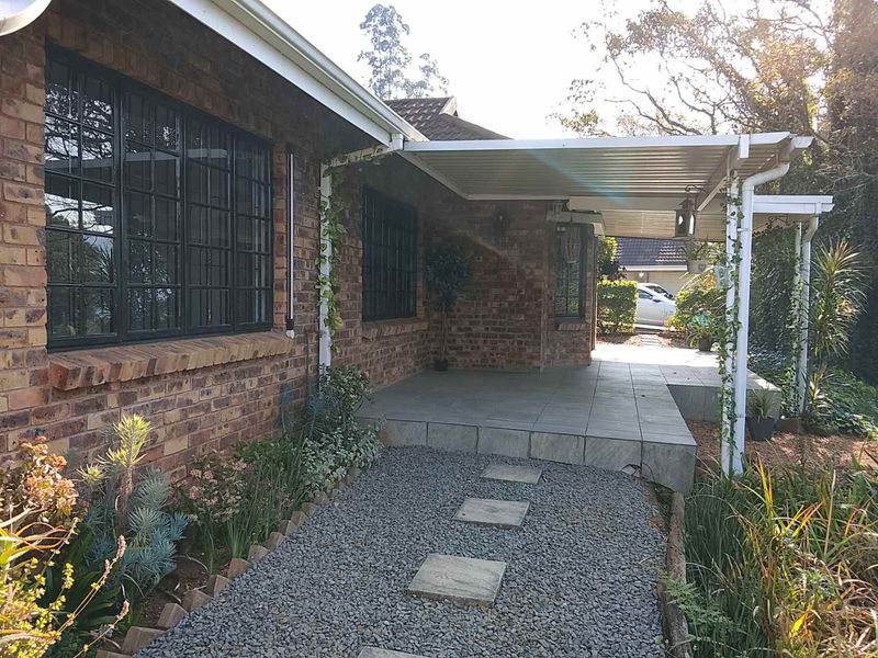 A covered brick-walled patio area featuring tiled flooring, metal support structures, and an adjacent gravel pathway leading to the entrance.