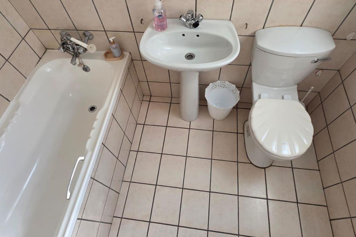 A functional bathroom featuring a pedestal basin, toilet, and bathtub with full-height wall tiling and tiled flooring.