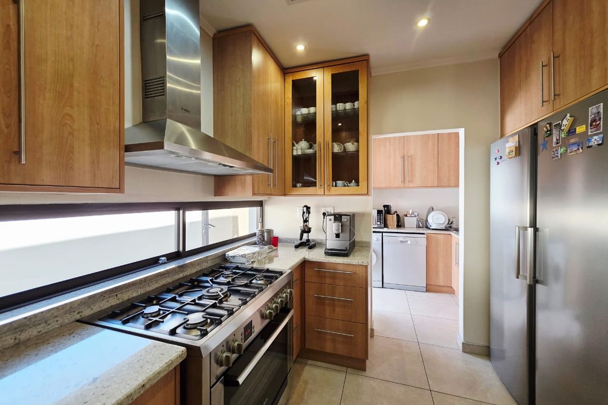 Well-appointed kitchen featuring granite countertops, gas stove with stainless steel extractor, and ample wooden cabinetry, with an adjoining scullery area.