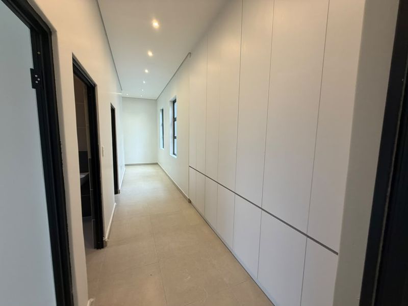 A bright, modern hallway featuring extensive built-in floor-to-ceiling cabinetry, neutral tiled flooring, and recessed downlighting.