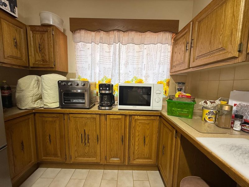 A functional kitchen featuring traditional wooden cabinetry, tiled backsplash, and durable tiled flooring, offering a classic aesthetic with ample storage space.