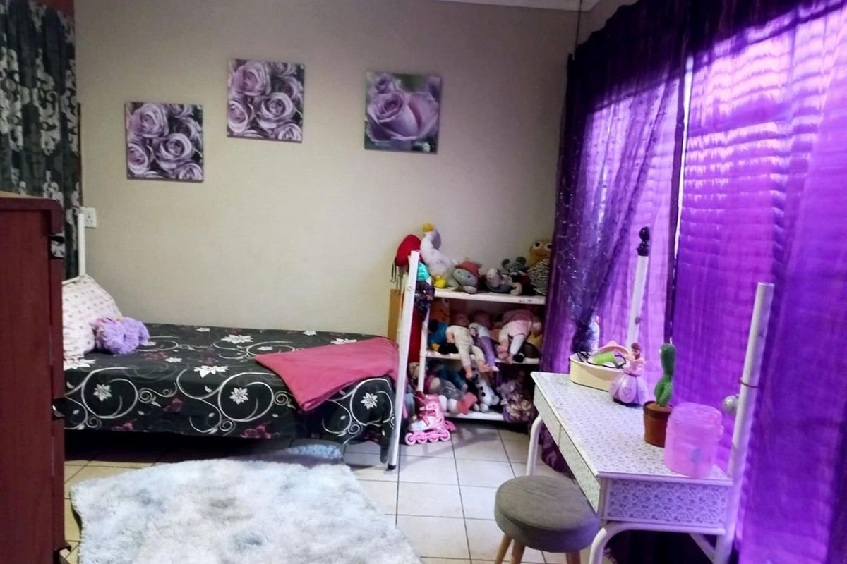 A bedroom featuring tiled flooring and large windows with purple curtains, providing a functional space for rest.