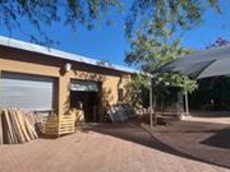 Exterior view of a garage building featuring roller shutter doors, a paved driveway, and an adjacent shade cloth carport structure.