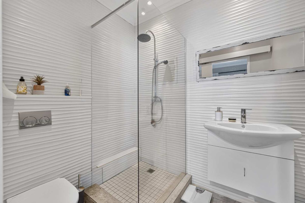 Modern bathroom featuring a walk-in shower with a glass screen, rain shower head, vanity basin with storage, and contemporary textured wall tiling.