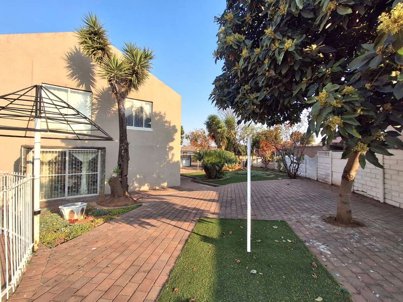 A spacious rear exterior area featuring paved pathways, artificial turf sections, and a secure boundary wall, providing a functional outdoor space.