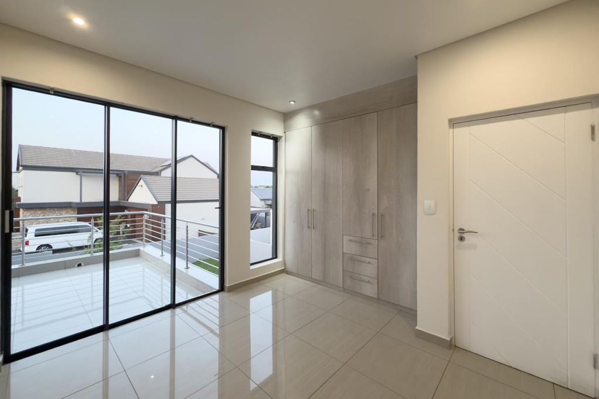 A bright bedroom featuring large glass sliding doors leading to a balcony, built-in wooden cabinetry, and polished floor tiles.