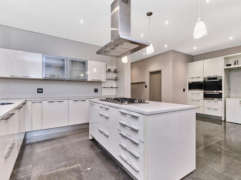 Modern kitchen featuring a central island with gas hob, stainless steel extractor, built-in appliances, high-gloss cabinetry, and polished stone floor tiles.