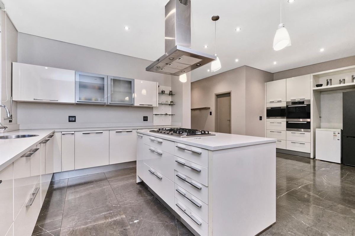 Modern kitchen featuring a central island with gas hob, stainless steel extractor, built-in appliances, high-gloss cabinetry, and polished stone floor tiles.