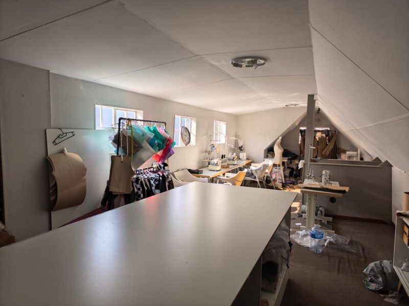 An attic-style office space featuring sloped ceilings, multiple windows, and carpeted flooring, currently utilized as a creative workspace.