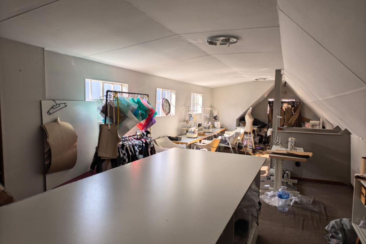 An attic-style office space featuring sloped ceilings, multiple windows, and carpeted flooring, currently utilized as a creative workspace.
