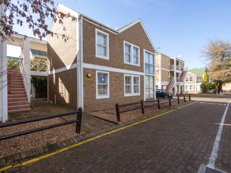 Exterior view of a multi-story brick apartment complex featuring paved driveway access and external staircases.