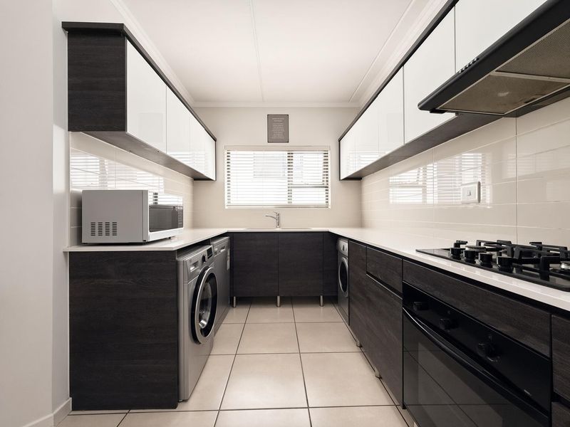 Modern galley-style kitchen featuring dark wood cabinetry, white countertops, integrated gas hob, oven, extractor fan, and tiled flooring with ample storage space.