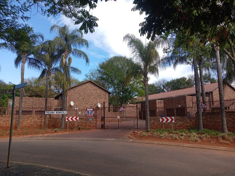 Street view of the Fraland Woonstelle apartment complex, featuring a brick facade, secure gated entrance, and mature palm trees.