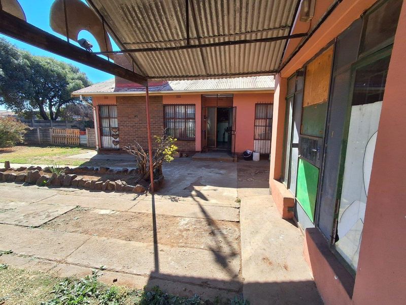 Rear exterior view of the property featuring a covered patio area, brick facade, and garden space with significant maintenance required.