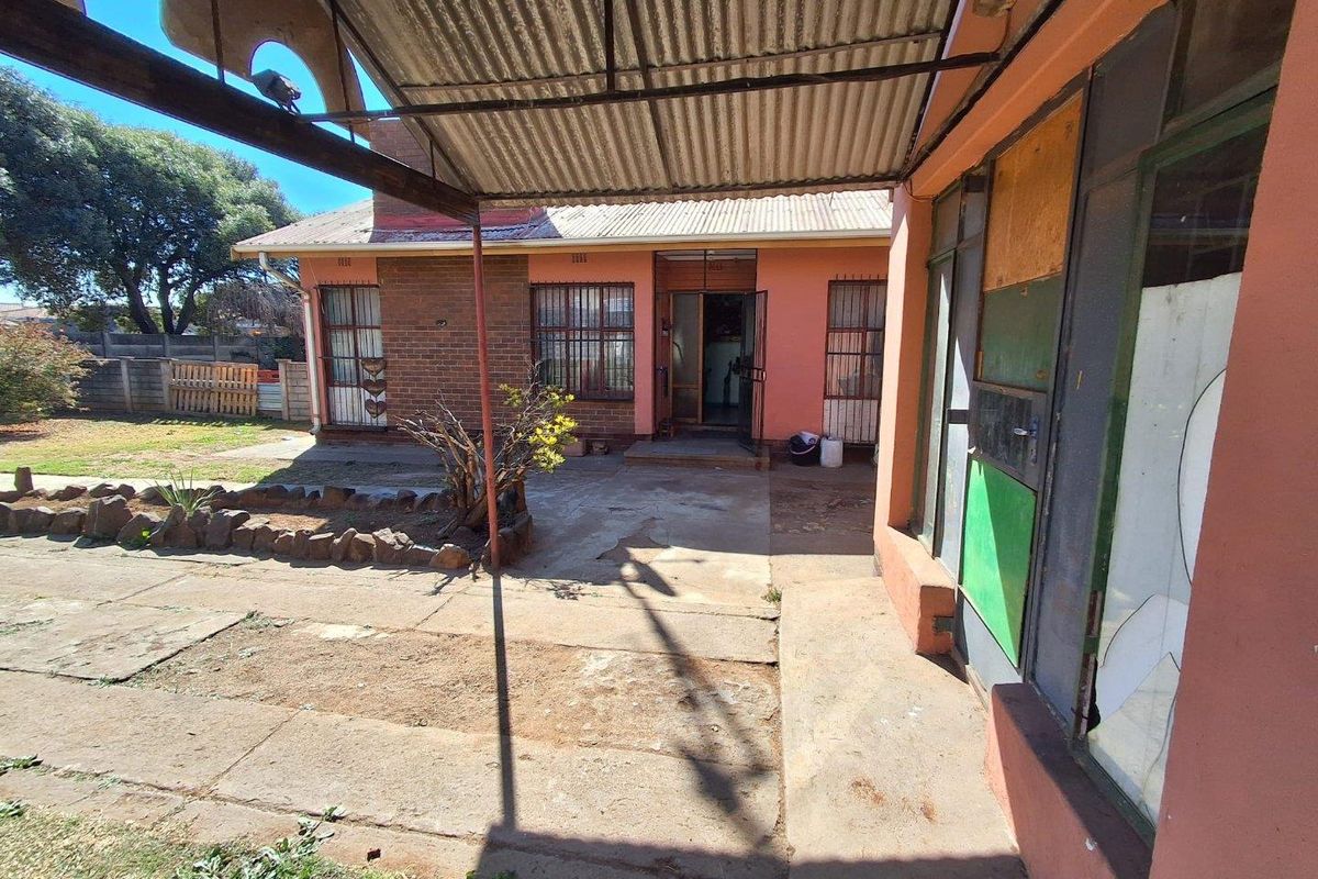 Rear exterior view of the property featuring a covered patio area, brick facade, and garden space with significant maintenance required.