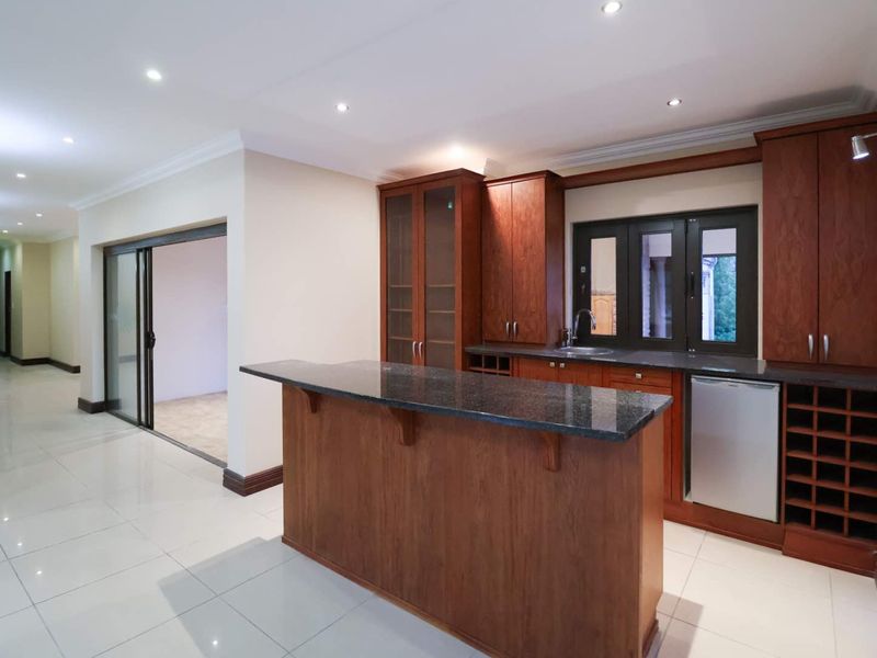 A clean, modern kitchen featuring dark wood cabinetry, granite countertops, tiled floors, and recessed lighting, with an open-plan layout and sliding door access.