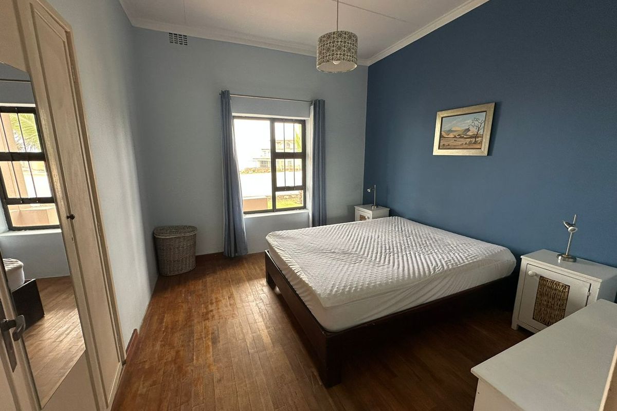 A bedroom featuring timber flooring, a large window with security bars, and a feature wall, providing a functional and well-lit sleeping space.