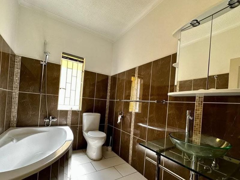 A functional bathroom featuring a corner bathtub, glass vessel sink with vanity shelf, and tiled finishes throughout.