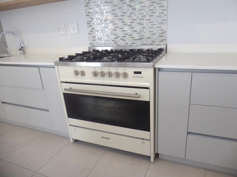 Modern kitchen featuring a cream-colored gas range, mosaic tile backsplash, sleek handleless cabinetry, and white quartz countertops with an undermount sink.