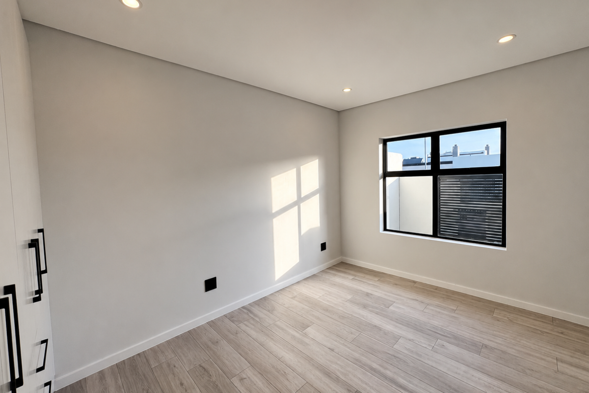 A bright, modern bedroom featuring light wood-look flooring, recessed ceiling lighting, and built-in cabinetry with sleek black hardware.