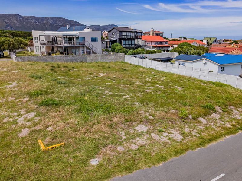 An elevated aerial view of a vacant residential plot situated in a developed neighborhood, featuring street access and established boundary fencing.