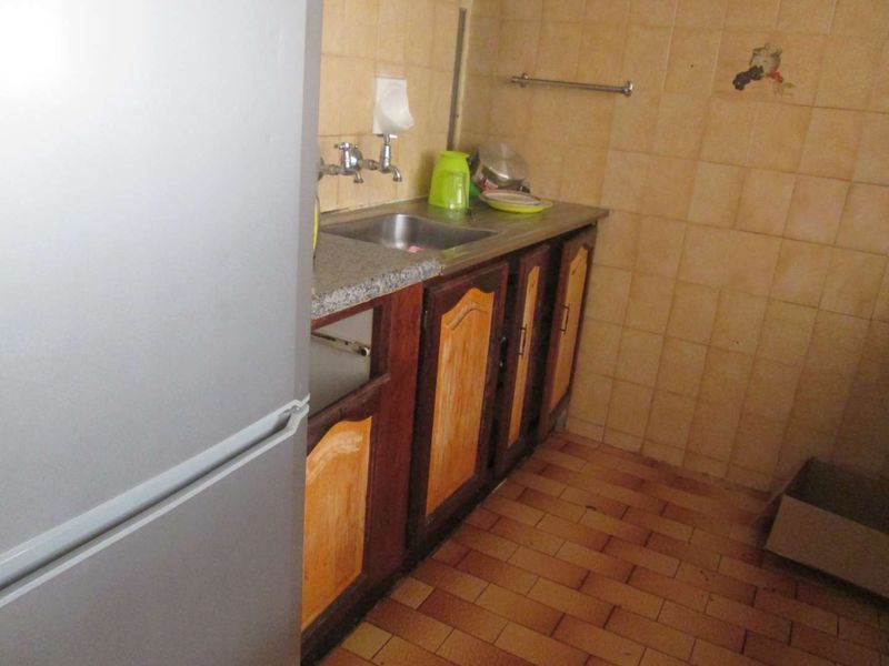 A dated kitchen area featuring built-in wooden cabinetry, a stainless steel sink, and tiled wall finishes, requiring modernization to improve functionality and aesthetic appeal.