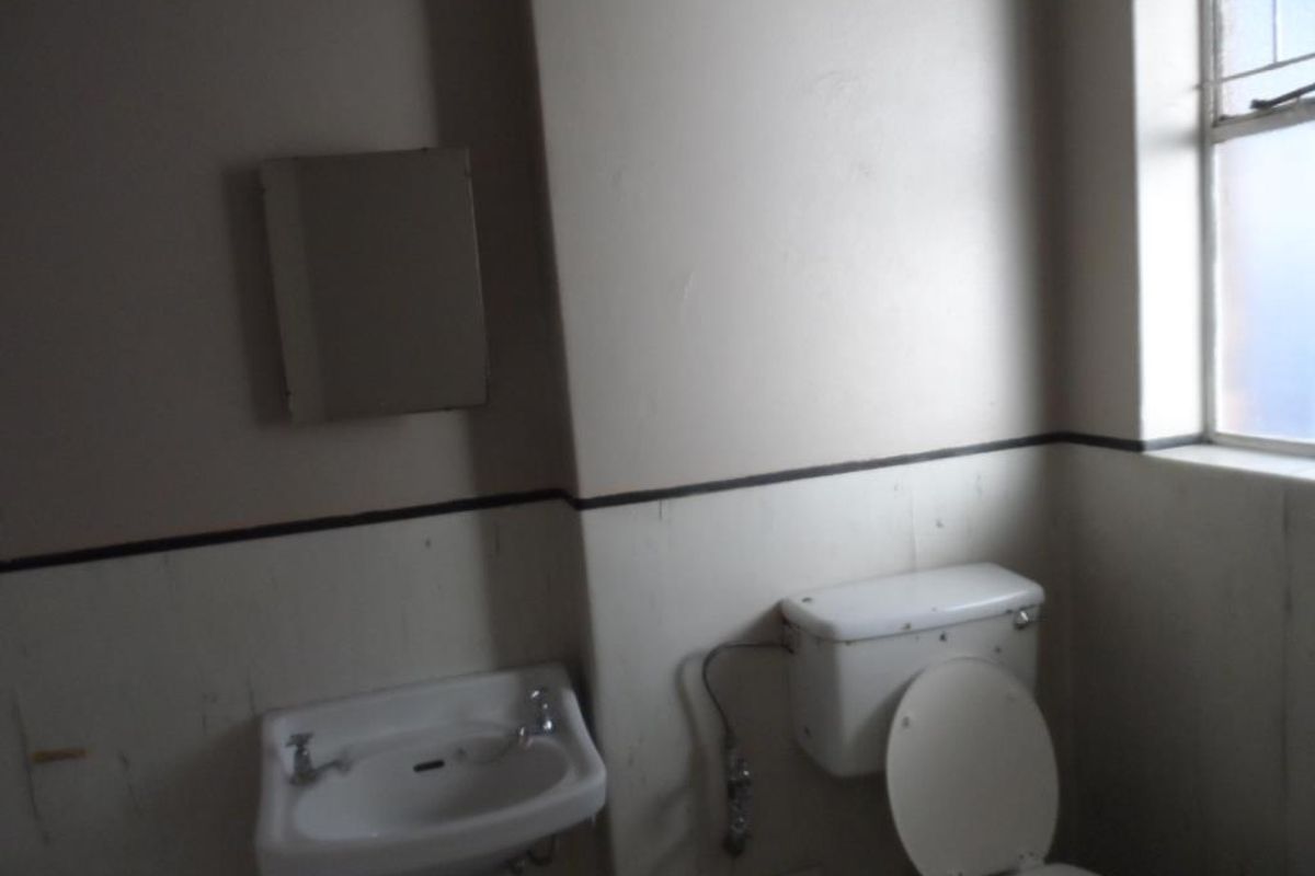 A dated bathroom featuring a wall-mounted basin, toilet, and mirror, requiring cosmetic updates to improve the overall aesthetic and functionality.