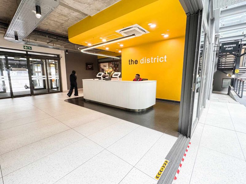 Modern commercial reception area featuring a bright yellow accent wall, sleek white reception desk, tiled flooring, and contemporary exposed ceiling design.