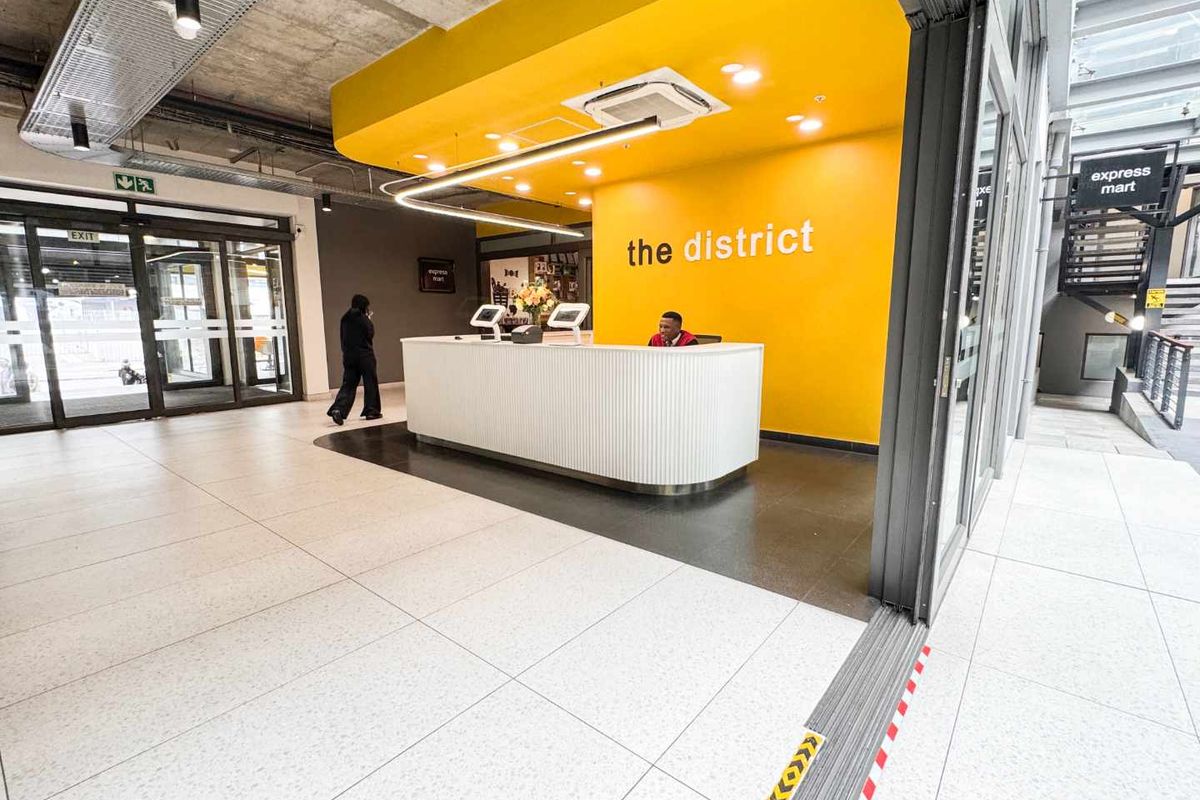 Modern commercial reception area featuring a bright yellow accent wall, sleek white reception desk, tiled flooring, and contemporary exposed ceiling design.