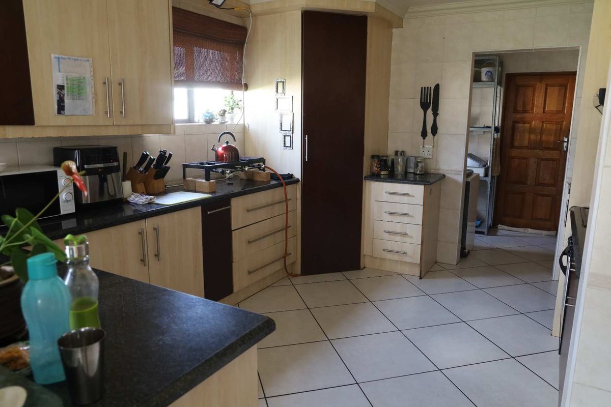 A functional kitchen featuring light wood-tone cabinetry, dark laminate countertops, tiled flooring, and an adjacent scullery area with a wooden door.